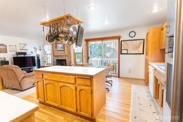 kitchen featuring white dishwasher, a brick fireplace, light countertops, and light wood finished floors