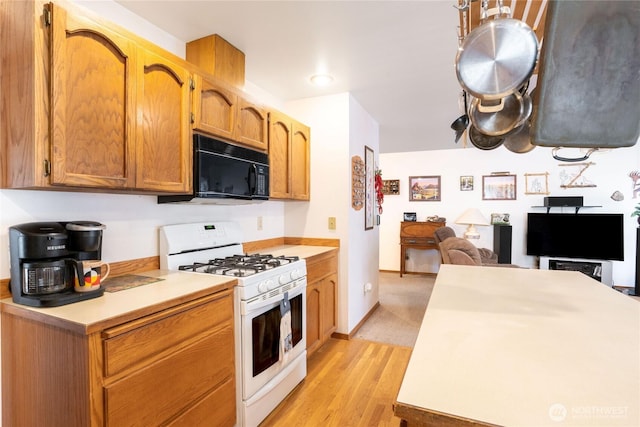 kitchen with white range with gas cooktop, black microwave, light wood-type flooring, light countertops, and open floor plan