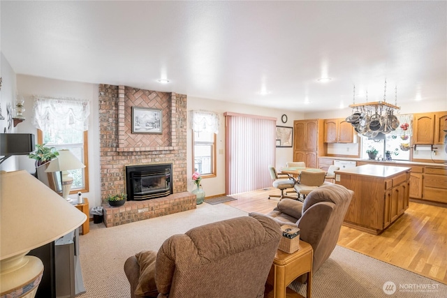 living room featuring light wood-type flooring, a healthy amount of sunlight, a notable chandelier, and a brick fireplace