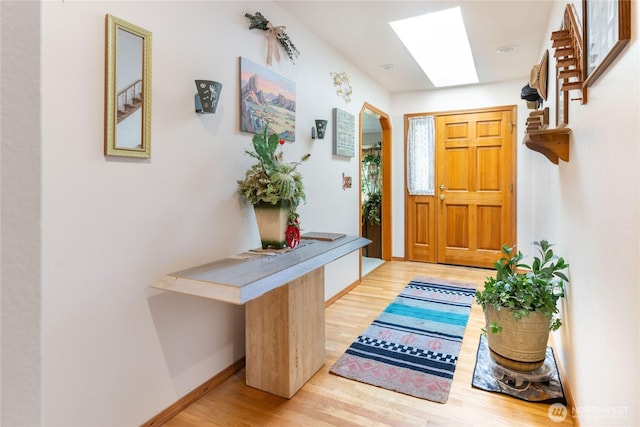 entrance foyer featuring arched walkways, light wood finished floors, baseboards, and a skylight