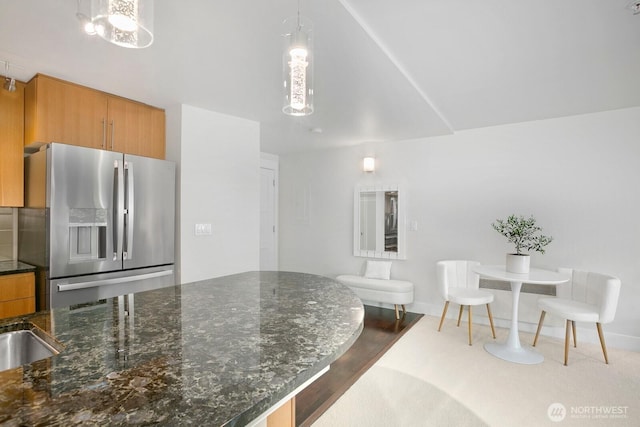 kitchen with decorative backsplash, pendant lighting, brown cabinets, stainless steel fridge with ice dispenser, and dark stone countertops