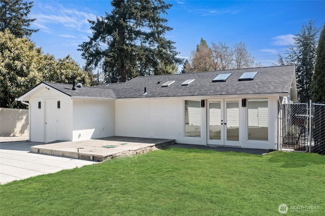back of house featuring fence, roof with shingles, french doors, a patio area, and a lawn