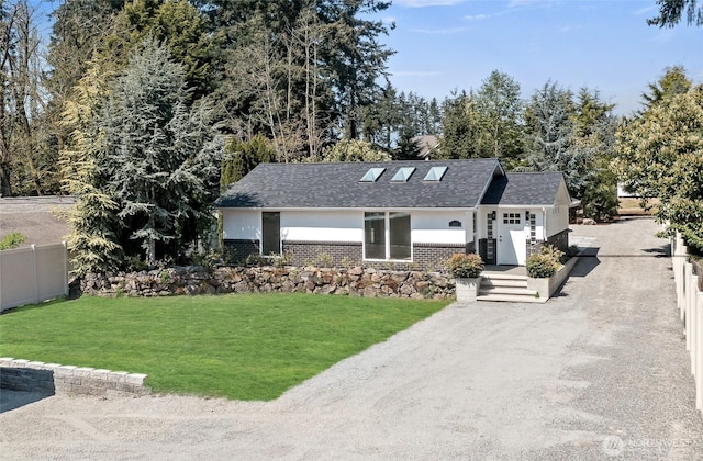 view of front of home with dirt driveway, brick siding, fence, a front lawn, and a shingled roof