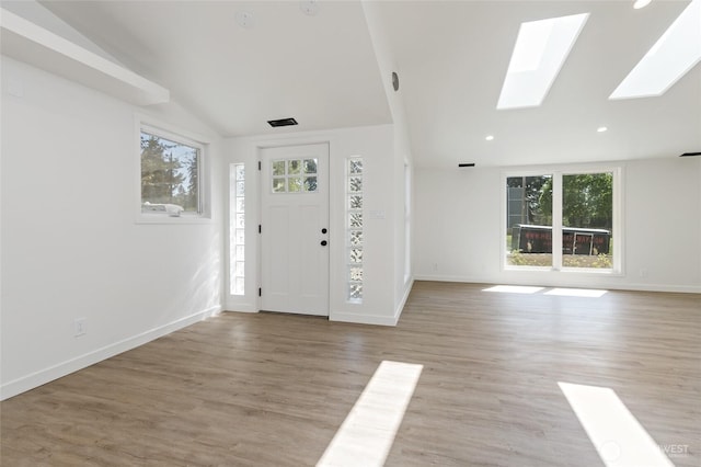 foyer entrance featuring baseboards, lofted ceiling with skylight, light wood-style flooring, and a wealth of natural light