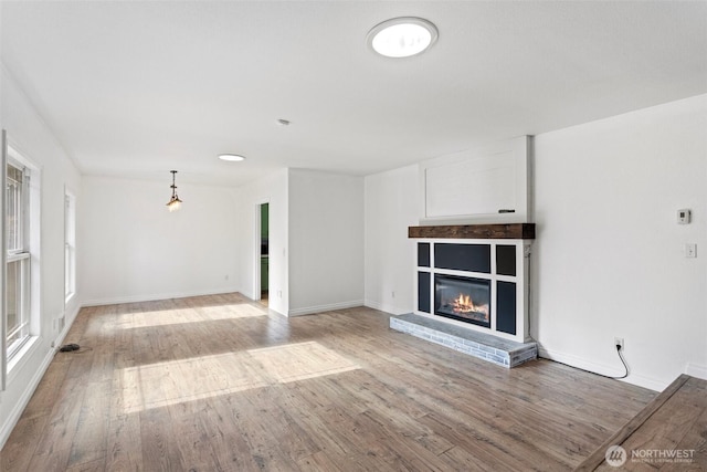 unfurnished living room with baseboards, light wood-type flooring, and a glass covered fireplace