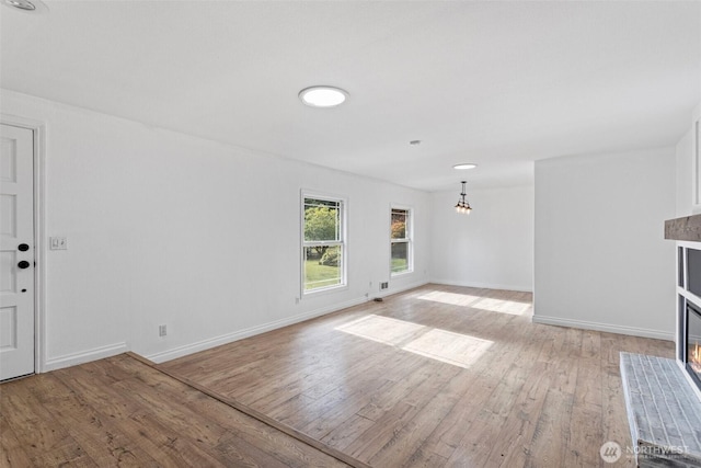 unfurnished living room featuring baseboards, light wood finished floors, a chandelier, and a glass covered fireplace