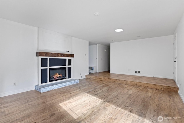 unfurnished living room featuring light wood finished floors, baseboards, a glass covered fireplace, and visible vents