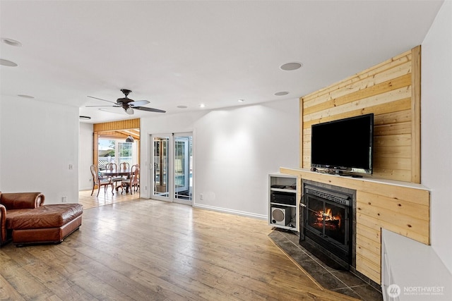 living area with wood-type flooring, baseboards, a ceiling fan, and a lit fireplace