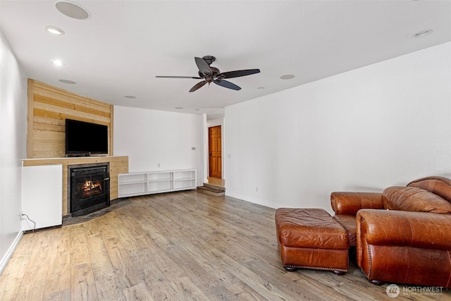 unfurnished room with wood finished floors, ceiling fan, a tiled fireplace, and baseboards