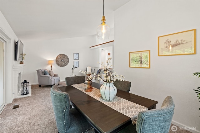 carpeted dining room featuring baseboards, a brick fireplace, and visible vents