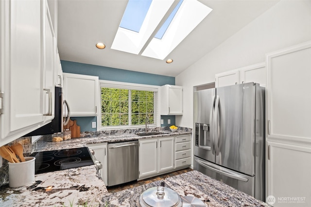 kitchen featuring a sink, white cabinetry, lofted ceiling with skylight, stainless steel appliances, and light stone counters