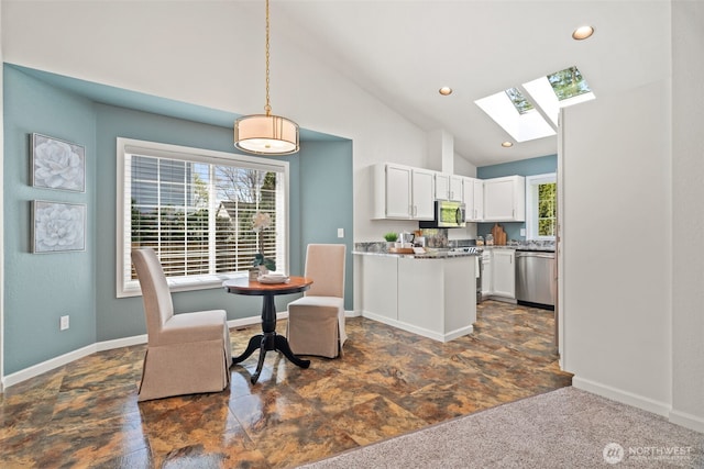 kitchen featuring baseboards, vaulted ceiling with skylight, white cabinets, appliances with stainless steel finishes, and pendant lighting