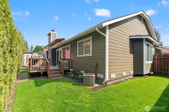 rear view of property with a deck, a chimney, fence, and a lawn