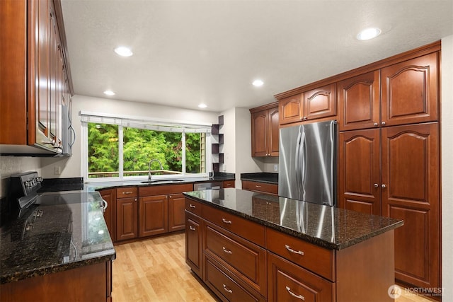 kitchen with dark stone countertops, appliances with stainless steel finishes, a sink, and light wood-style floors