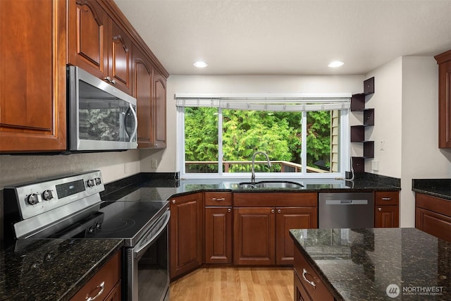 kitchen featuring dark stone countertops, light wood finished floors, a sink, and stainless steel appliances