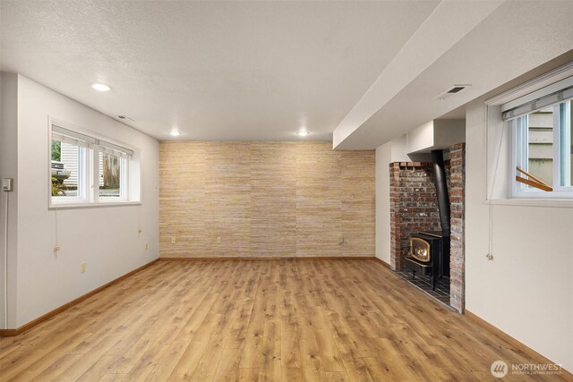 basement with baseboards, a textured ceiling, a wood stove, visible vents, and light wood finished floors