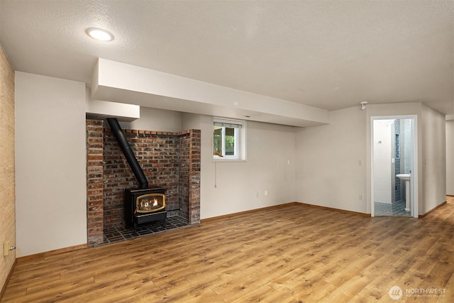 basement featuring a textured ceiling, wood finished floors, a wood stove, and baseboards