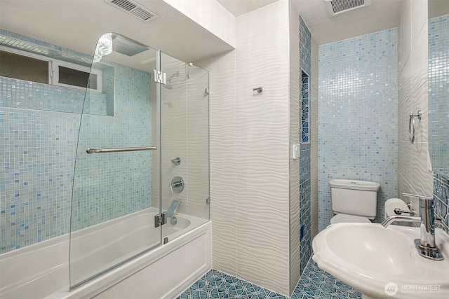 full bath featuring visible vents, tile walls, a sink, and enclosed tub / shower combo