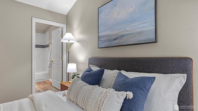 bedroom featuring ensuite bathroom, a textured wall, and wood finished floors