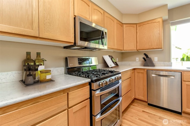 kitchen featuring light brown cabinetry, stainless steel appliances, light wood finished floors, and light countertops