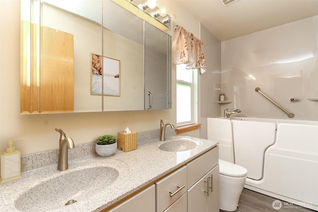 full bathroom with double vanity, a sink, toilet, and a tub to relax in
