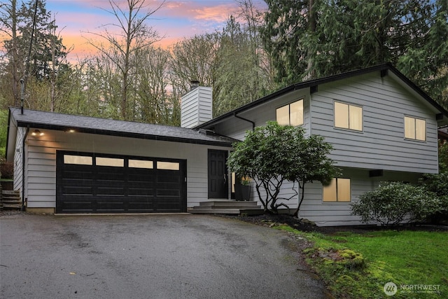 tri-level home with an attached garage, a chimney, and driveway