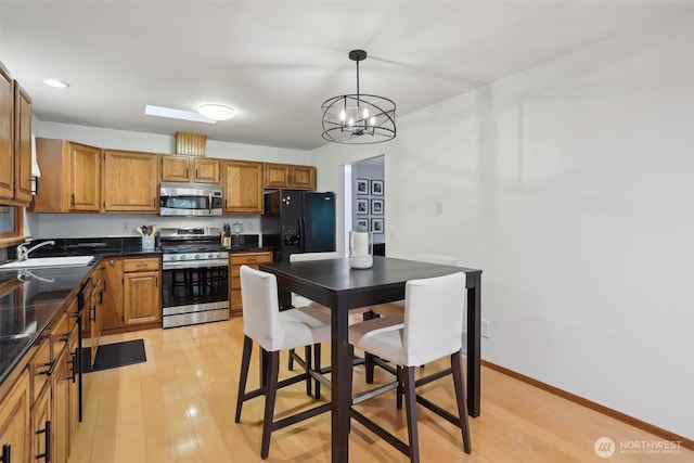 kitchen with stainless steel appliances, light wood finished floors, a sink, and dark countertops