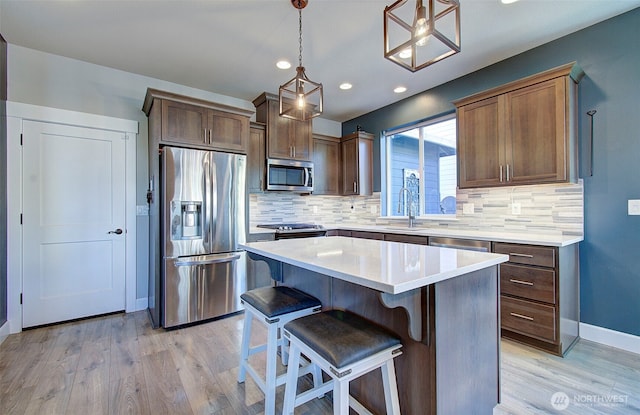 kitchen with light wood finished floors, light countertops, stainless steel appliances, backsplash, and a kitchen island