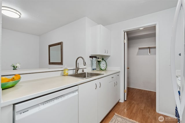 kitchen with white cabinets, dishwasher, a sink, light countertops, and light wood finished floors