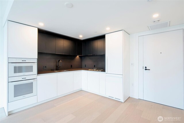 300 Virginia St Unit 1710, Seattle, WA 98101 - kitchen featuring white cabinets, decorative backsplash, light wood finished floors, double oven, and a sink