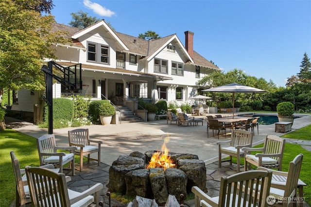 rear view of property with a patio area, a fire pit, an outdoor pool, and stairs