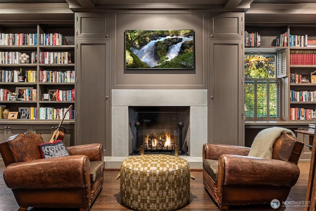living area featuring wood finished floors, built in features, and a lit fireplace