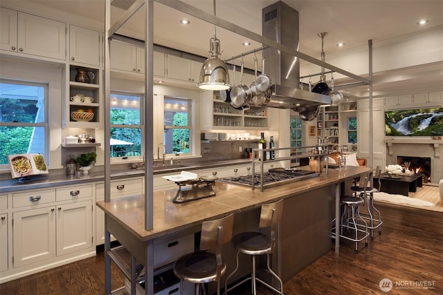 bar with stainless steel gas cooktop, dark wood-style floors, recessed lighting, island range hood, and a warm lit fireplace