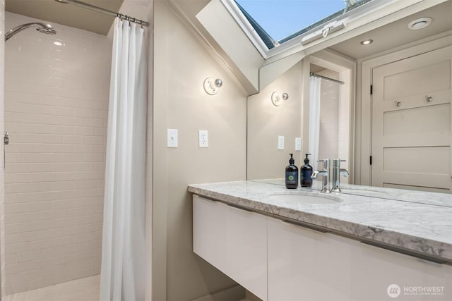 full bath with a skylight, vanity, and tiled shower