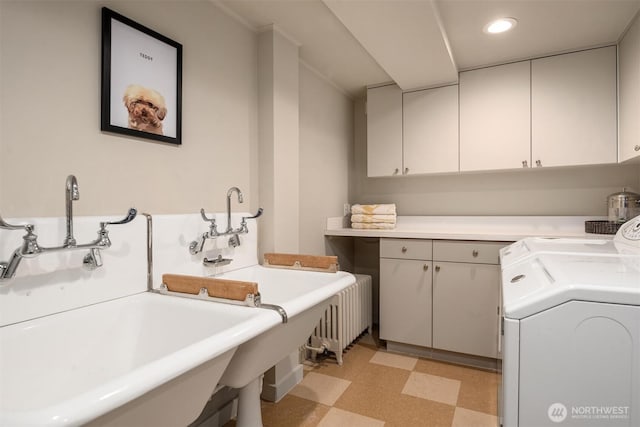 laundry area featuring a sink, radiator heating unit, cabinet space, light floors, and washer and dryer