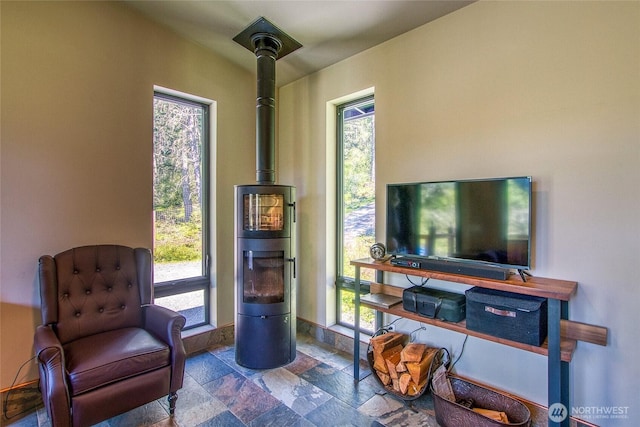 sitting room with a wood stove, a wealth of natural light, and stone tile flooring