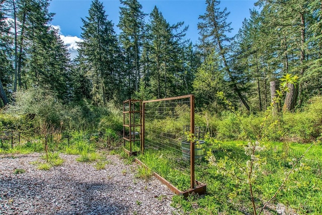 view of gate with a garden and a view of trees