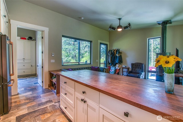 kitchen featuring stone finish floor, white cabinets, a wood stove, wooden counters, and freestanding refrigerator