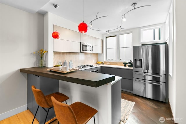 kitchen with a peninsula, backsplash, dark countertops, decorative light fixtures, and appliances with stainless steel finishes