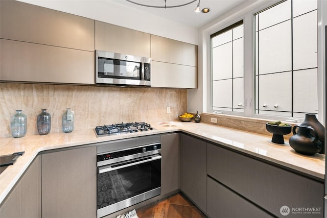 kitchen featuring appliances with stainless steel finishes, light stone counters, gray cabinets, a healthy amount of sunlight, and decorative backsplash