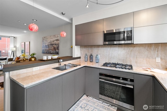 kitchen with tasteful backsplash, a peninsula, gray cabinetry, appliances with stainless steel finishes, and a sink