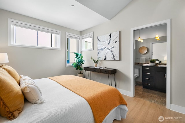 bedroom featuring baseboards, light wood finished floors, connected bathroom, and lofted ceiling