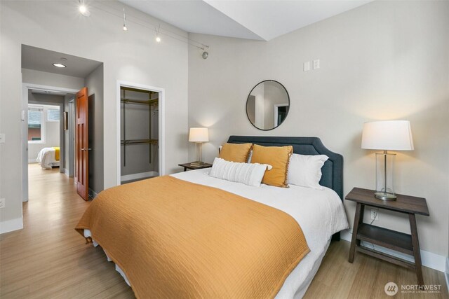 bedroom with baseboards, rail lighting, and wood finished floors