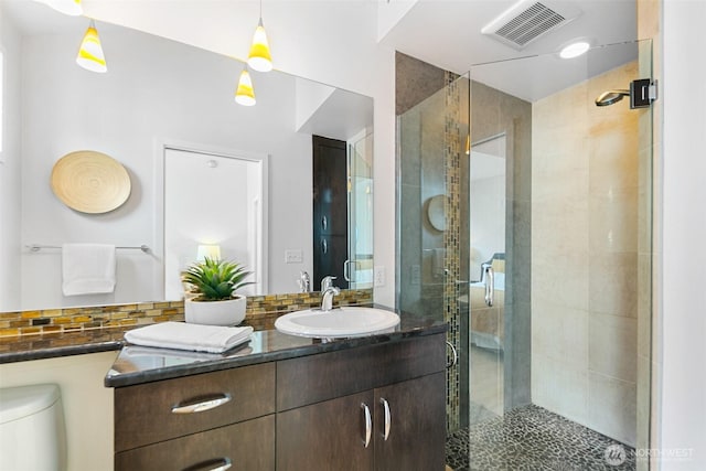 bathroom featuring vanity, visible vents, toilet, a stall shower, and backsplash