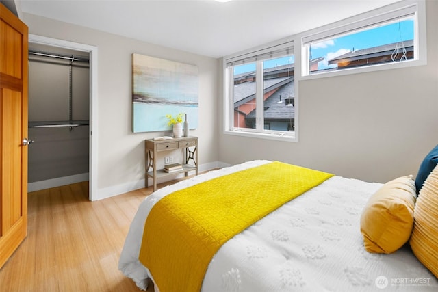 bedroom with a spacious closet, a closet, baseboards, and wood finished floors