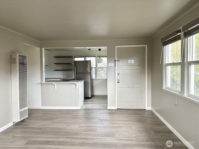 interior space with a peninsula, freestanding refrigerator, a heating unit, and light wood-style floors