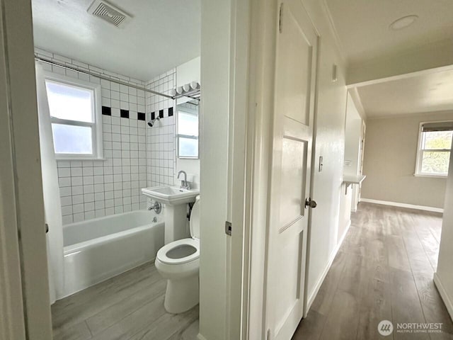 full bath with shower / washtub combination, visible vents, toilet, wood finished floors, and baseboards