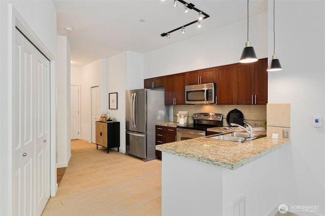 kitchen with hanging light fixtures, a sink, stainless steel appliances, a peninsula, and tasteful backsplash
