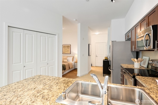kitchen with brown cabinets, light stone counters, appliances with stainless steel finishes, a sink, and light wood-type flooring