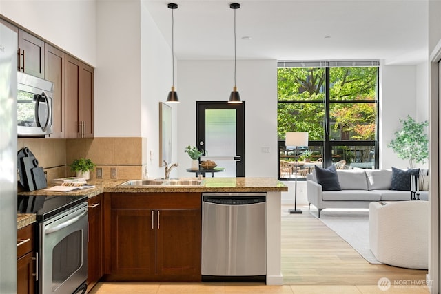 kitchen with appliances with stainless steel finishes, a sink, light countertops, a peninsula, and backsplash